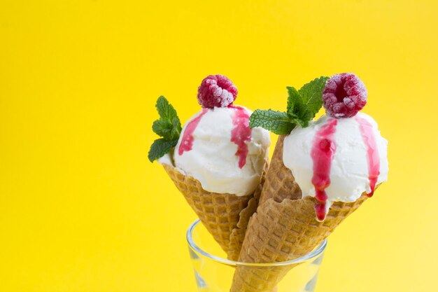 Primer plano sobre helado de vainilla en un cono de galleta con frambuesas sobre el fondo amarillo. Copie el espacio.