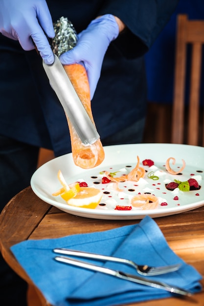 Foto primer plano sobre las manos del chef del restaurante italiano raspando virutas de rollo de salmón cocido en la placa