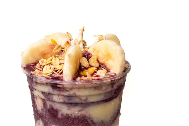 Primer plano sobre vaso de acai con plátano, granola y leche condensada aislado sobre fondo blanco.