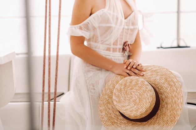 Primer plano de un sombrero de paja en manos de una novia sentada en un yate