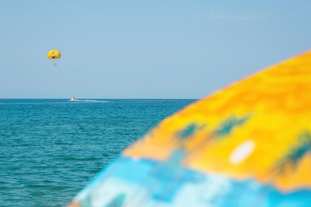 Primer plano de sombrilla de playa borrosa contra el mar y el fondo del cielo soleado. Sombrilla y parapente en el mar.