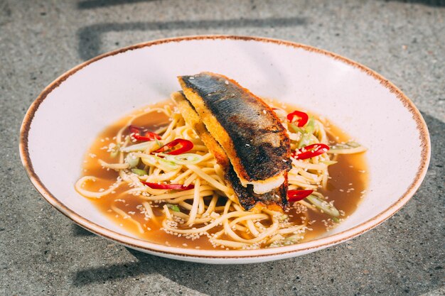 Primer plano de una sopa de macarrones con pescado y verduras servida en un tazón blanco