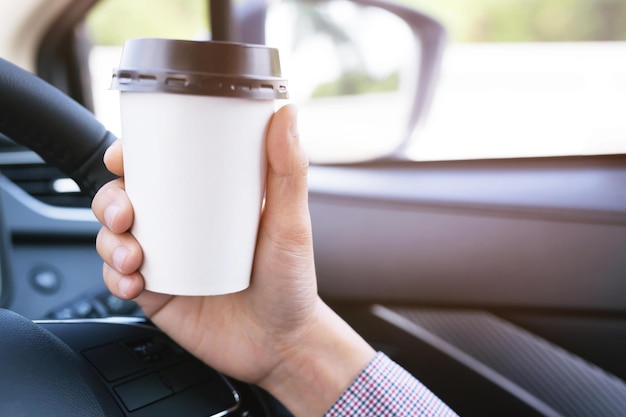 Primer plano sostenga una taza de café de papel para beber en el automóvil Bebida conceptual para refrescarse o ayudar a despertarse del sueño durante la conducción que puede causar un accidente automovilístico