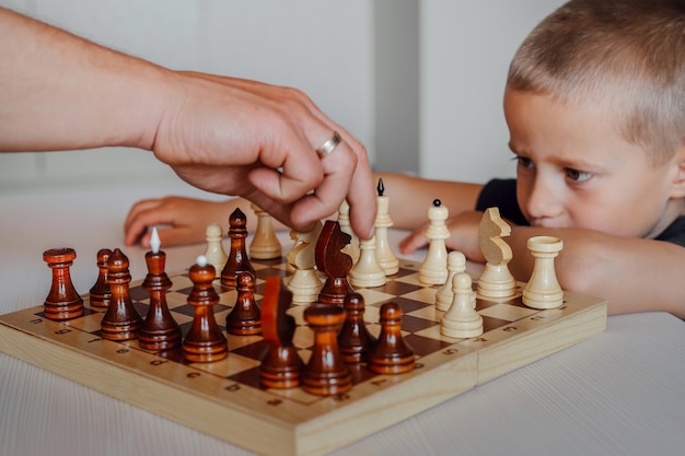 Primer plano de tablero de ajedrez, que juega un padre e hijo de fiesta. Un niño blanco vigila de cerca la mano de su padre.