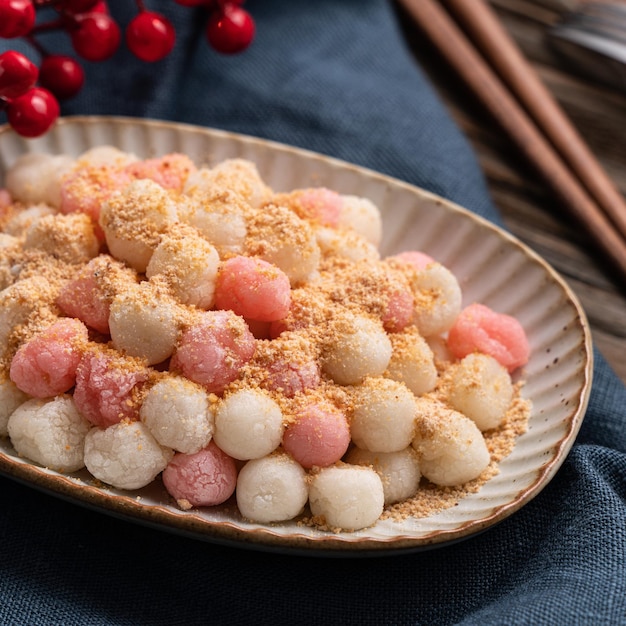 Primer plano de tangyuan rojo y blanco frito (tang yuan, bolas de masa hervida de arroz glutinoso) con polvo de maní en el fondo de la mesa de madera para la comida del festival del solsticio de invierno.