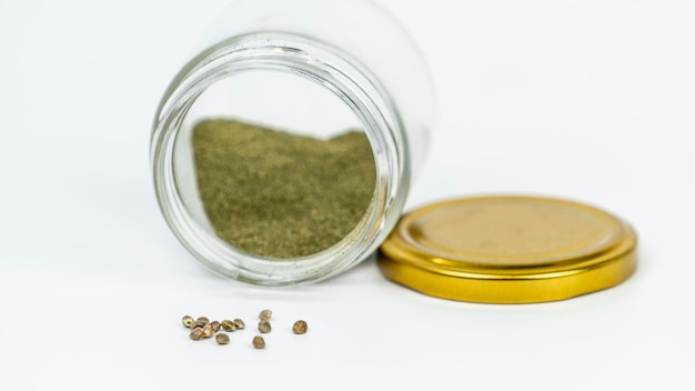 Primer plano de un tarro de cristal con semillas de hachís y cannabis aisladas sobre fondo blanco