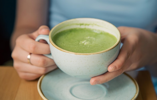 Primer plano de una taza con bebida de matcha verde en manos femeninas