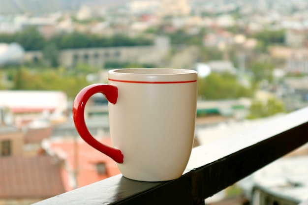 Primer plano de una taza de café en el balcón contra la vista borrosa de la ciudad