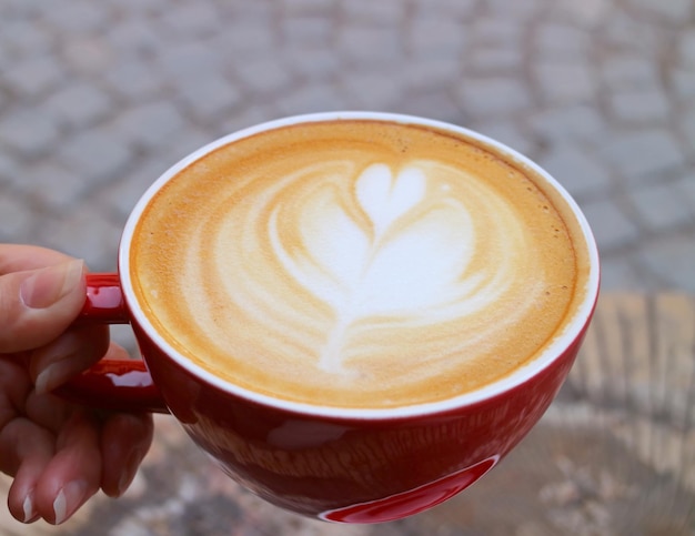 Primer plano de una taza de café capuchino caliente en la mano de la mujer