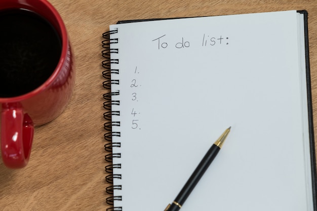 Primer plano de la taza de café con diario y bolígrafo