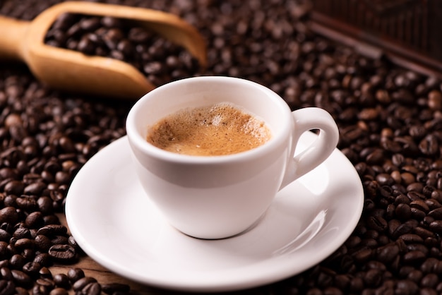 Primer plano de la taza de café expreso sobre granos de café tostados oscuros