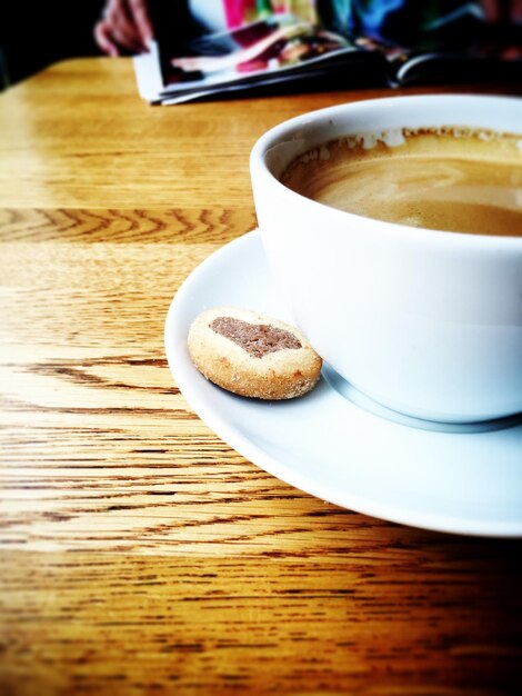 Foto primer plano de la taza de café y la galleta en el platillo en la mesa