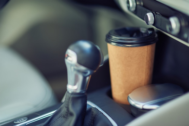 Primer plano de una taza de café de papel en el portavasos entre los asientos del coche moderno