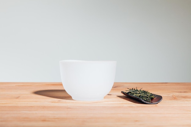 Primer plano de una taza de té de vidrio blanco sobre una mesa de madera con hojas de té secas sobre un fondo neutro