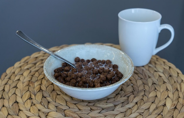 Primer plano de un tazón con cereal y leche y una taza de desayuno