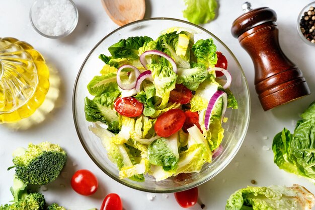 Primer plano de un tazón de vidrio de ensalada verde vegana saludable con hojas de enrejado, tomates y cebolla llenos de vitaminas Fondo blanco Vista superior Nutritivos y enzimas en hojas de ensalada pueden desintoxicarse