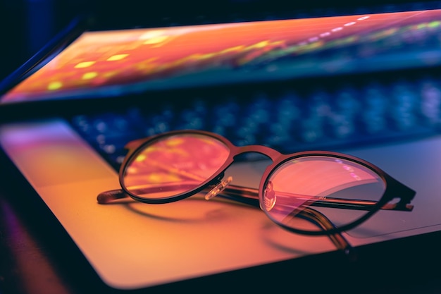 Un primer plano del teclado de la computadora portátil con colorida iluminación de neón y gafas