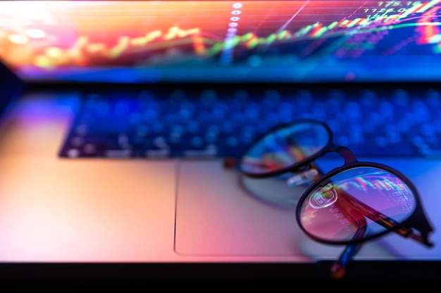 Un primer plano del teclado de la computadora portátil con colorida iluminación de neón y gafas