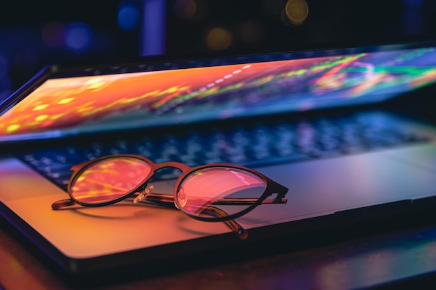 Un primer plano del teclado de la computadora portátil con colorida iluminación de neón y gafas