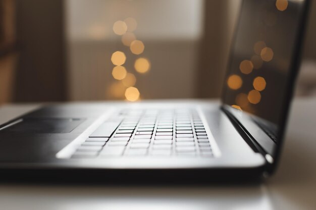 Primer plano del teclado de la computadora portátil con pantalla en blanco en una mesa con fondo de luces borrosas en la casa u oficina luz del sol moderna en la mañana