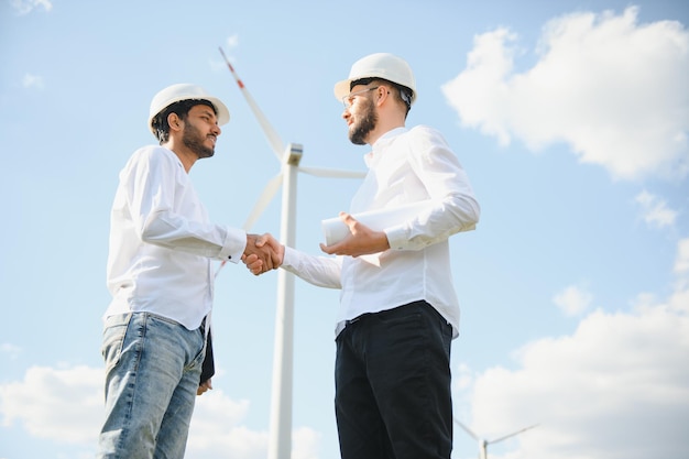 Primer plano de un técnico e inspector indio dándose la mano mientras está de pie en una granja con turbinas eólicas Concepto de trabajo en equipo de personas y energía ecológica