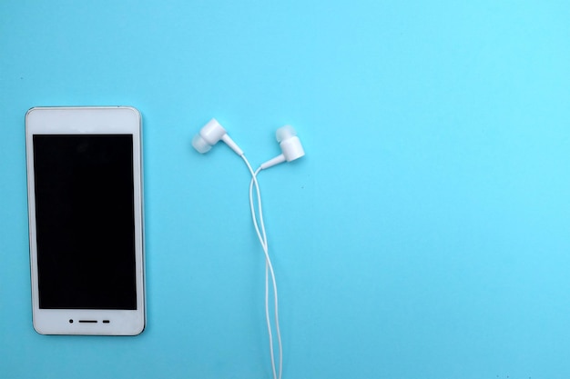 Foto primer plano de un teléfono inteligente con auriculares en el oído contra un fondo azul