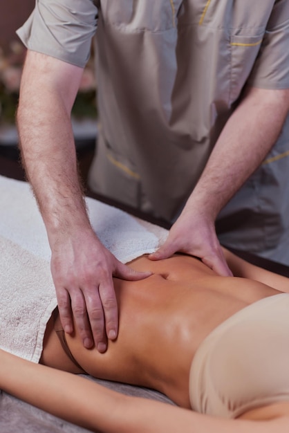 Primer plano de terapeuta haciendo masaje estomacal en mujer en spa contra fondo oscuro