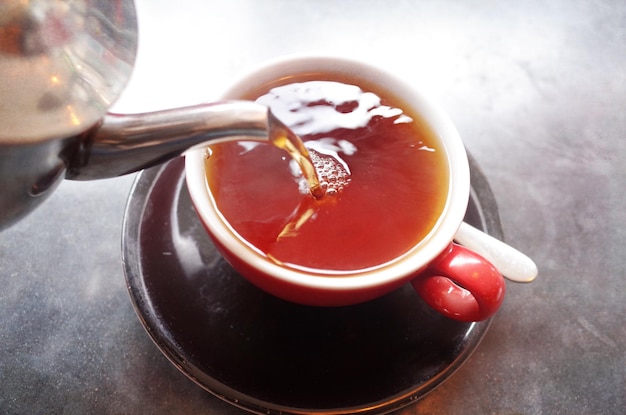 Primer plano de una tetera vertiendo té en una taza sobre la mesa