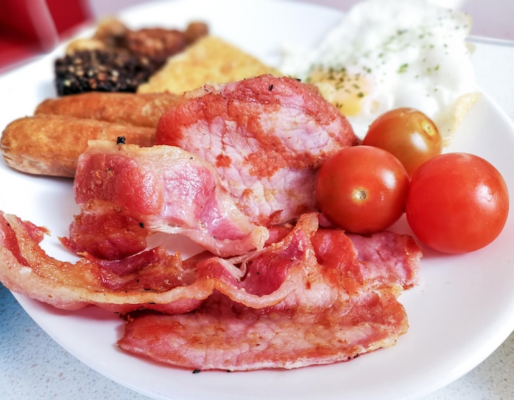 Foto primer plano de tocino con tomates cereza y huevo frito por salchichas en plato