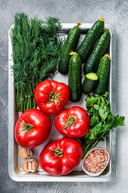 Primer plano de tomates rojos y pepinos verdes con hierbas en una bandeja de cocina. Fondo blanco. Vista superior.