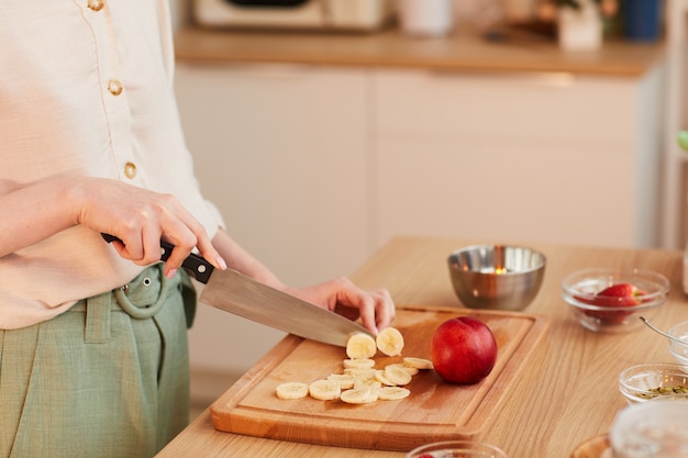 Primer plano de tonos cálidos de mujer irreconocible cortando frutas mientras prepara un desayuno saludable en la cocina