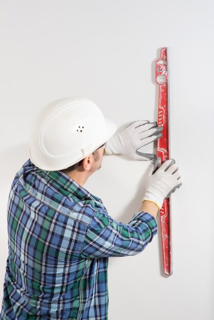 Primer plano de un trabajador de la construcción en un casco de seguridad inspeccionando una pared blanca lisa en un sitio de construcción