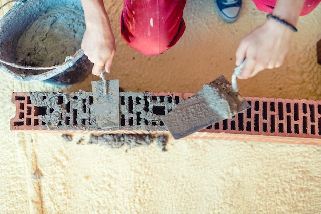 Primer plano de un trabajador de la construcción construyendo paredes y fijando ladrillos con mortero y espátula