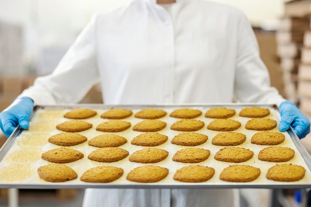 Primer plano del trabajador de la fábrica de alimentos que sostiene la bandeja con galletas