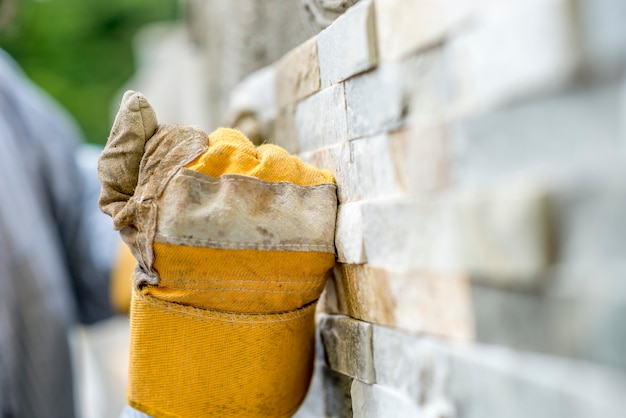 Primer plano de trabajador manual en guantes de protección alicatar una pared con azulejos ornamentales