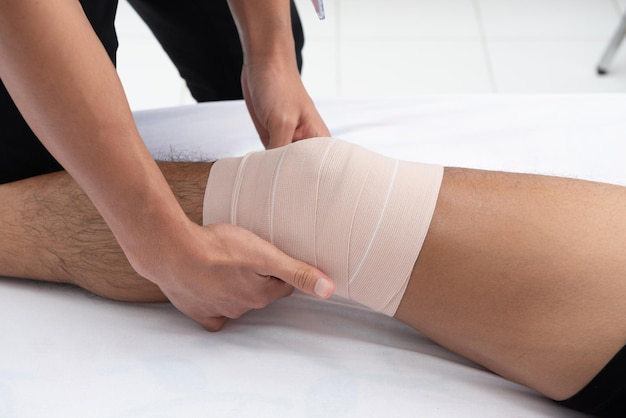 Foto primer plano de un trabajador de la salud envolviendo un vendaje en la rodilla de un hombre