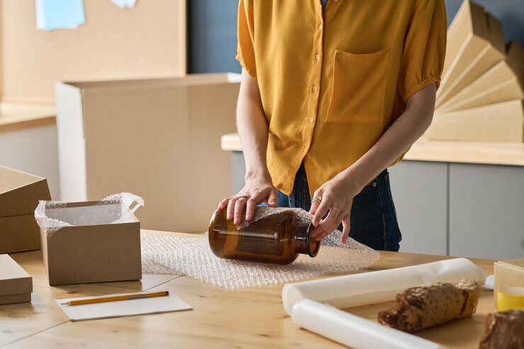 Foto primer plano de una trabajadora que envuelve un frasco de vidrio en un paquete para empacarlo en la caja para la entrega