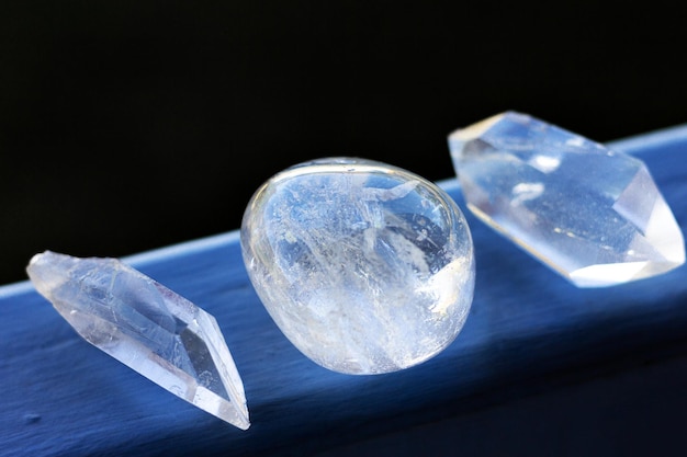 Foto primer plano de tres cristales de cuarzo claros que descansan sobre una superficie azul plana con fondo oscuro