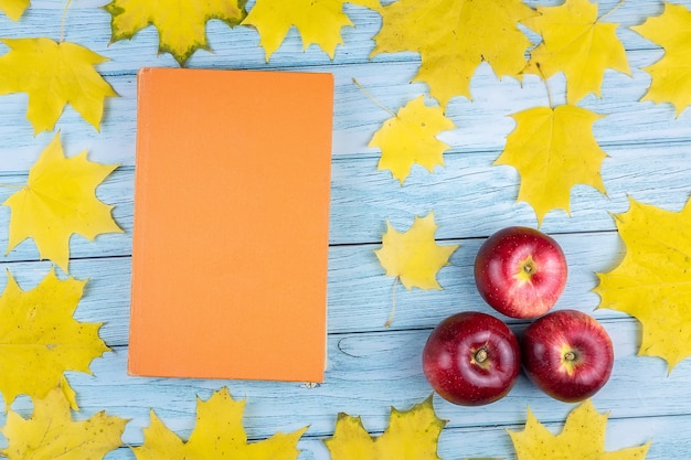 Foto primer plano de tres manzanas rojas y un viejo libro con hojas de arce