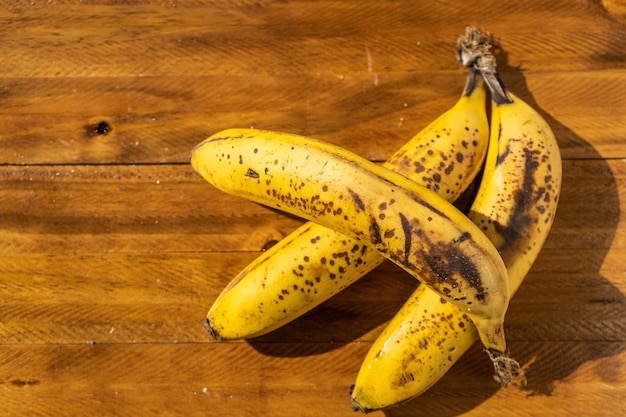 Primer plano de tres plátanos maduros sobre una tabla de madera. Frutas tropicales y saludables.