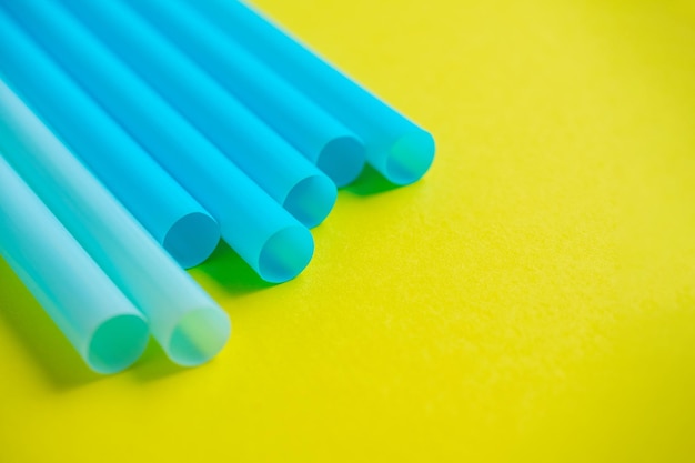 Foto primer plano de tubos de cóctel de plástico de color azul sobre un fondo amarillo.