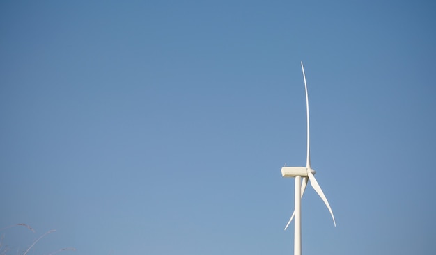 Primer plano de una turbina de molino de viento y palas que generan electricidad sobre un fondo de cielo azul. Concepto de producción de energía limpia y ecológica.