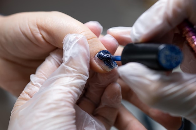 Primer plano de la uña en la que se aplica el esmalte de gel azul con un cepillo