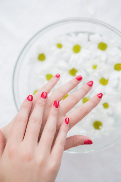 Primer plano de uñas pintadas de rojo y tazón de flores en manos spa