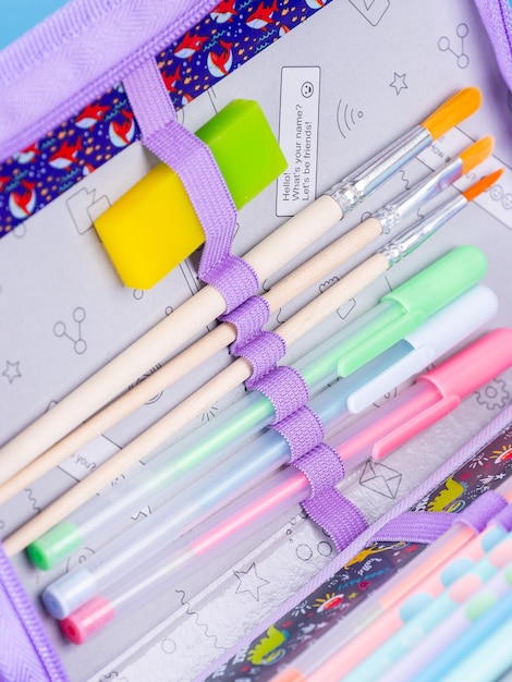 Primer plano de útiles escolares en estuche de lápices sobre fondo azul con trazado de recorte