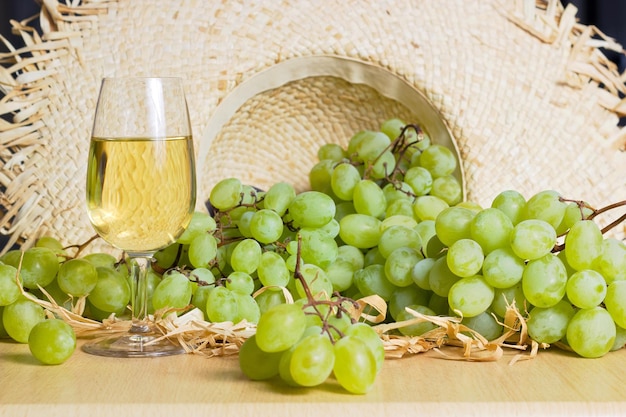 Primer plano de uvas y vaso de vino en la mesa contra un sombrero de mimbre