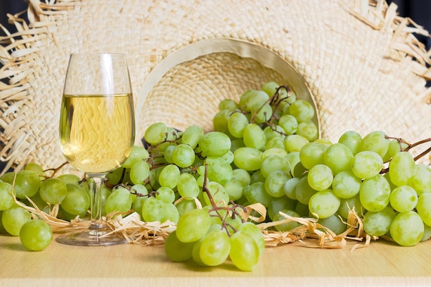 Foto primer plano de uvas y vaso de vino en la mesa contra un sombrero de mimbre