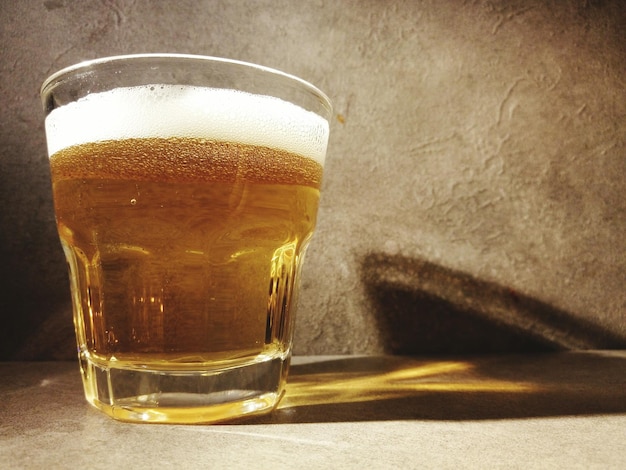 Primer plano de un vaso de cerveza en la mesa contra la pared