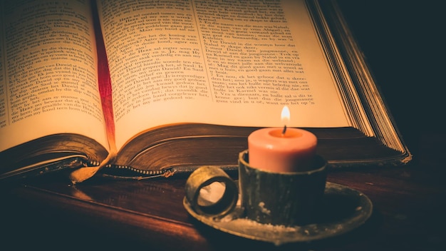 Primer plano de una vela encendida y una biblia en la mesa en el cuarto oscuro