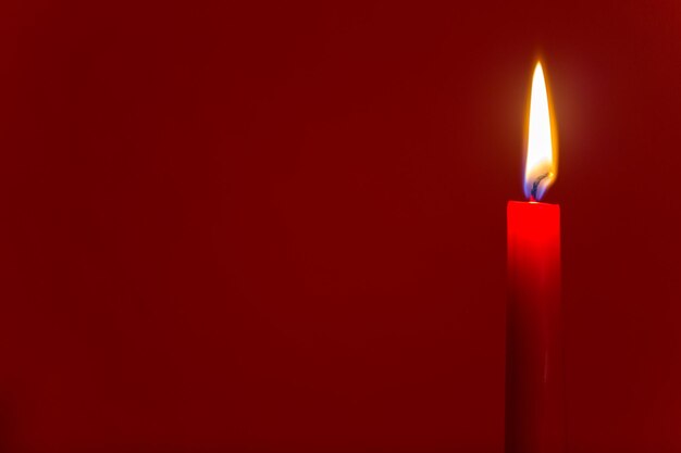 Primer plano de una vela iluminada contra un fondo rojo